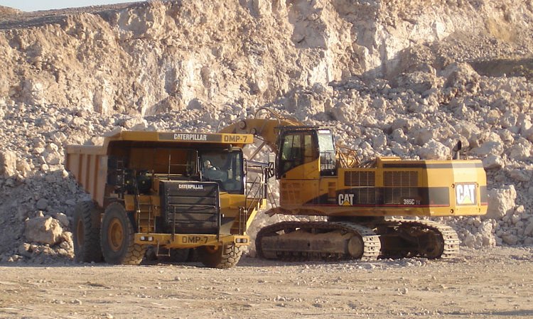 A Caterpillar dump truck being filled with limestone in the plant's quarry, by a Caterpillar tracked back-hoe excavator.